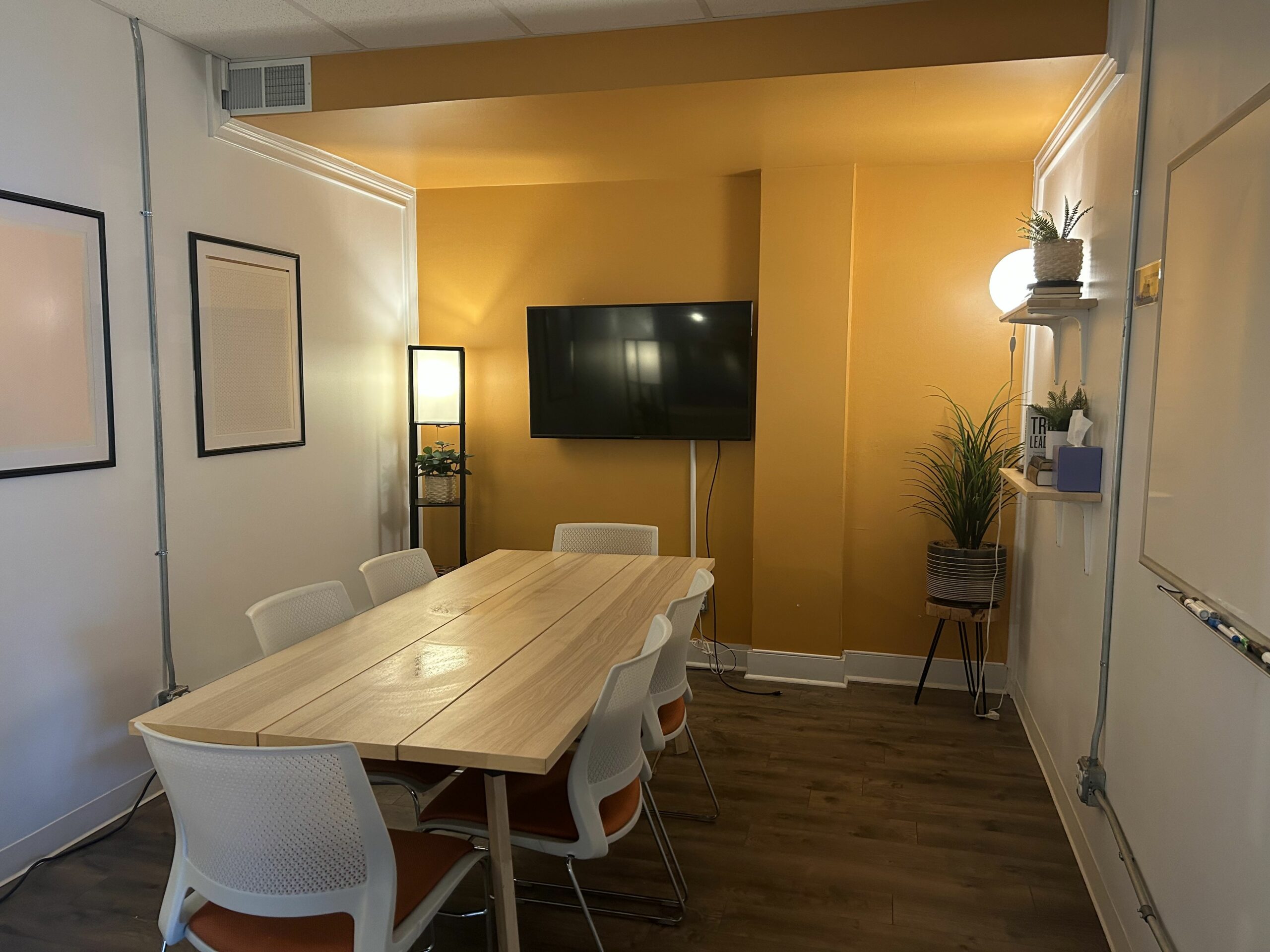 6 person meeting room with orange wall, TV, and whiteboard